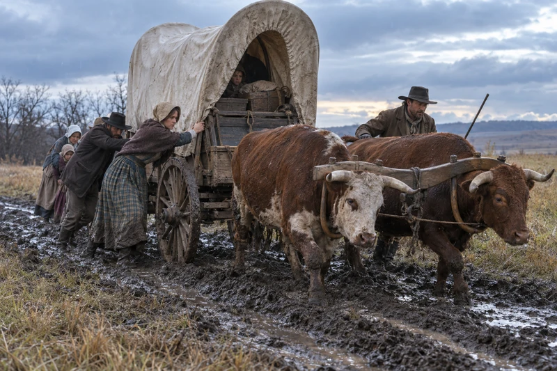Emigrants steady a wagon as yoked oxen pull through muddy Iowa ruts.