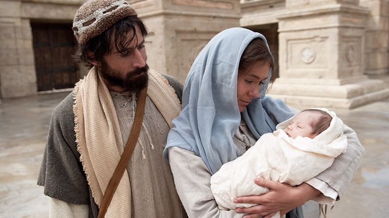 Mary holding the infant Jesus beside Joseph outside the temple in the Church Bible video.