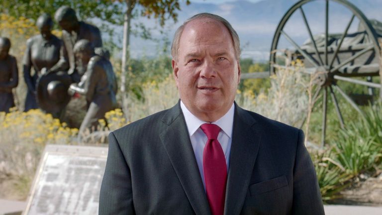 Elder Ronald A. Rasband beside a handcart pioneer monument.